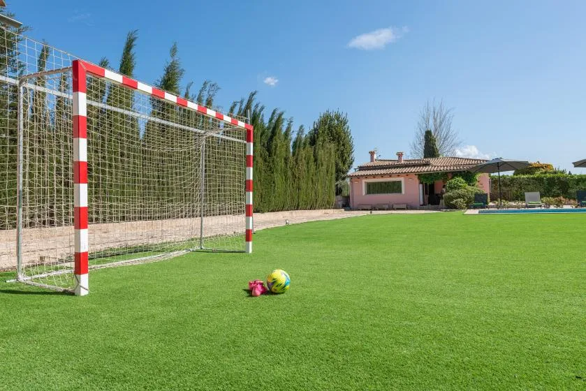 A grassy sports field with a soccer goal and ball in front of a house.
