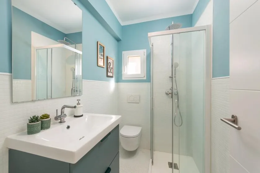 A bright bathroom with a sink, wall-mounted toilet, and glass shower.