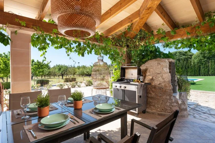 An outdoor dining area under a wooden pergola, with a table and grill.