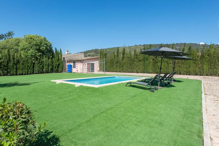 A swimming pool sits beside a broad lawn, with loungers and an umbrella nearby.