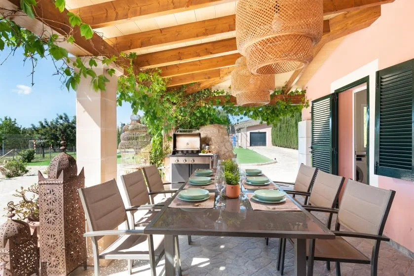 A covered outdoor dining area with a long table and chairs beside the house.