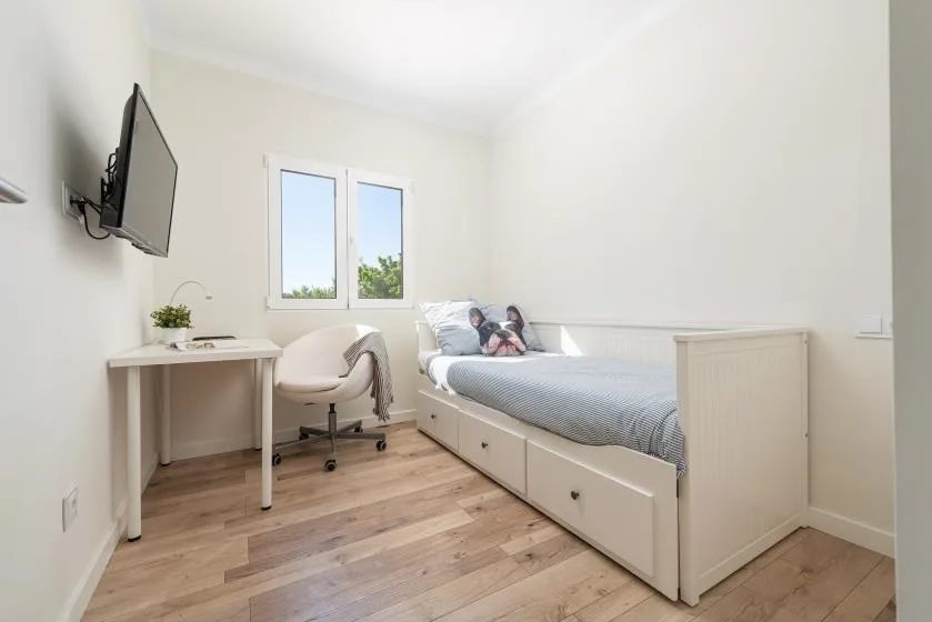 A bright bedroom with a bed, desk, and chair beside a window.