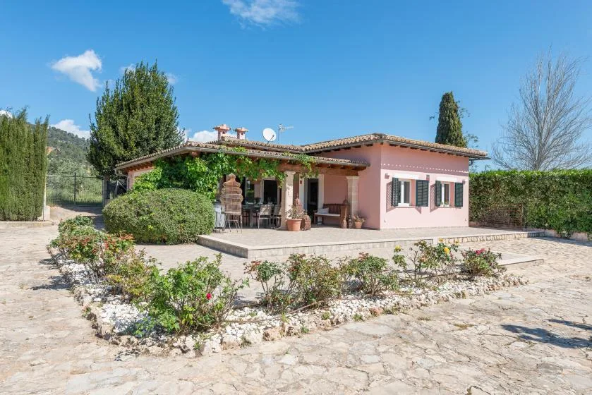 Una casa rosa con patio cubierto se encuentra junto a un patio de piedra.