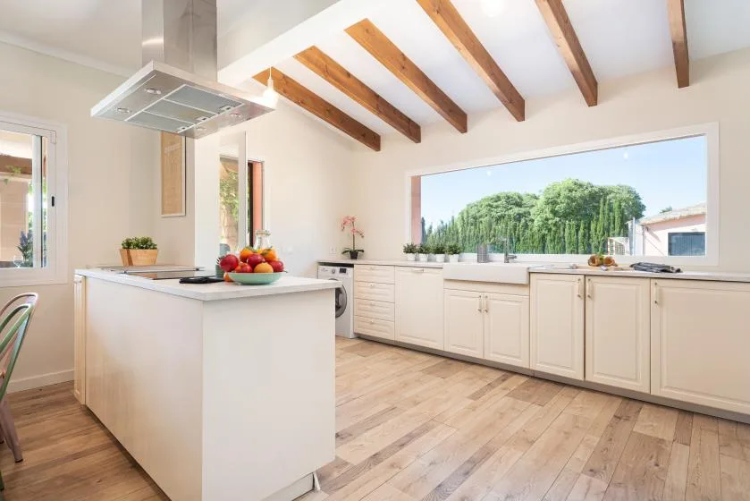 A bright kitchen with a central island, white cabinetry, and exposed ceiling beams.