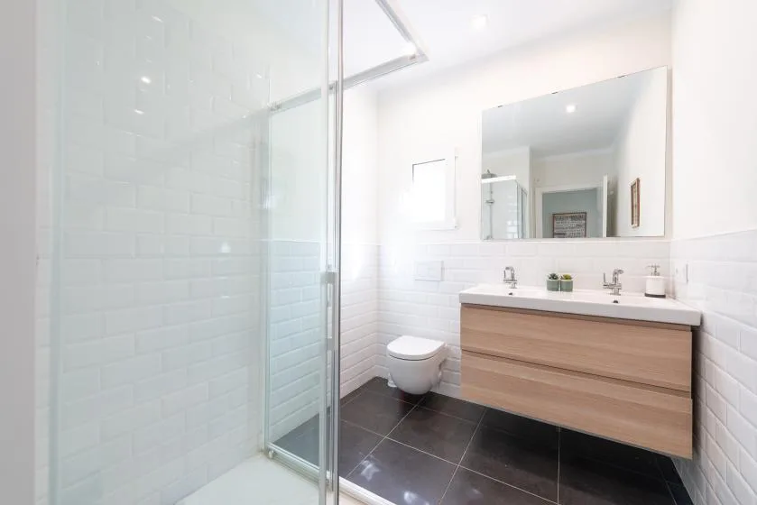 A bright bathroom with a glass shower, wall-mounted toilet, and wood-toned vanity.