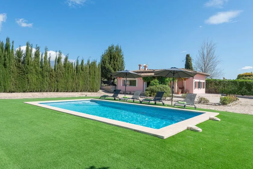 Una piscina al aire libre está sobre un césped verde frente a una casa.