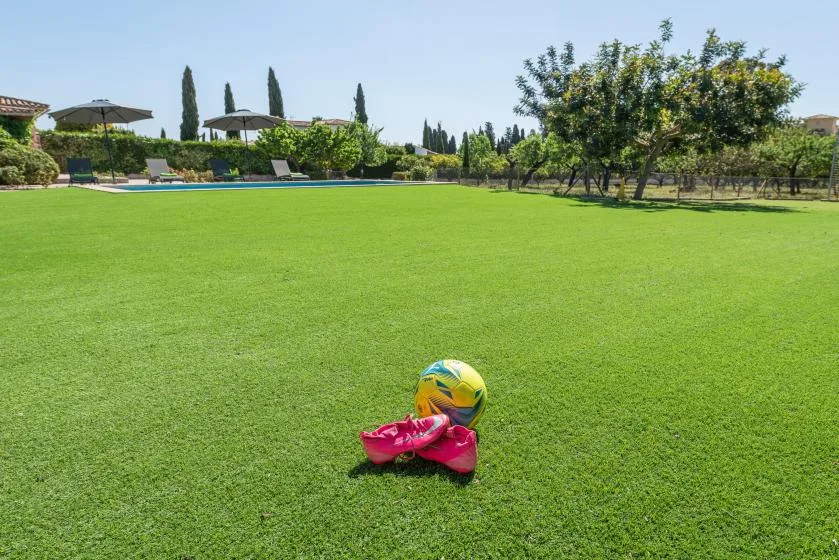 A broad green lawn with a colorful ball and a pair of shoes in the foreground.