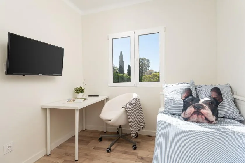A bright bedroom with a bed, desk, and window.