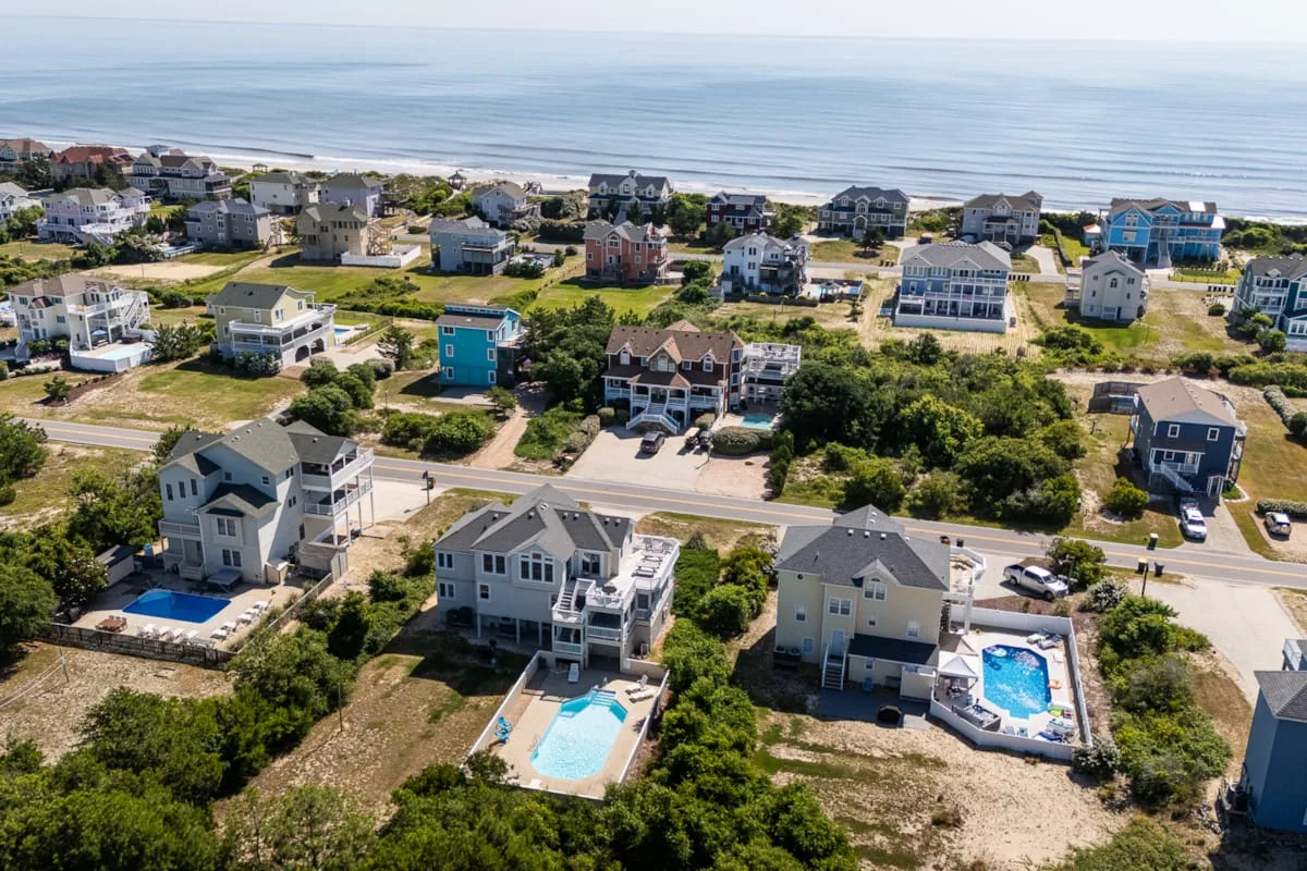 Vista aérea de casas costeras junto a una playa de arena y aguas tranquilas.