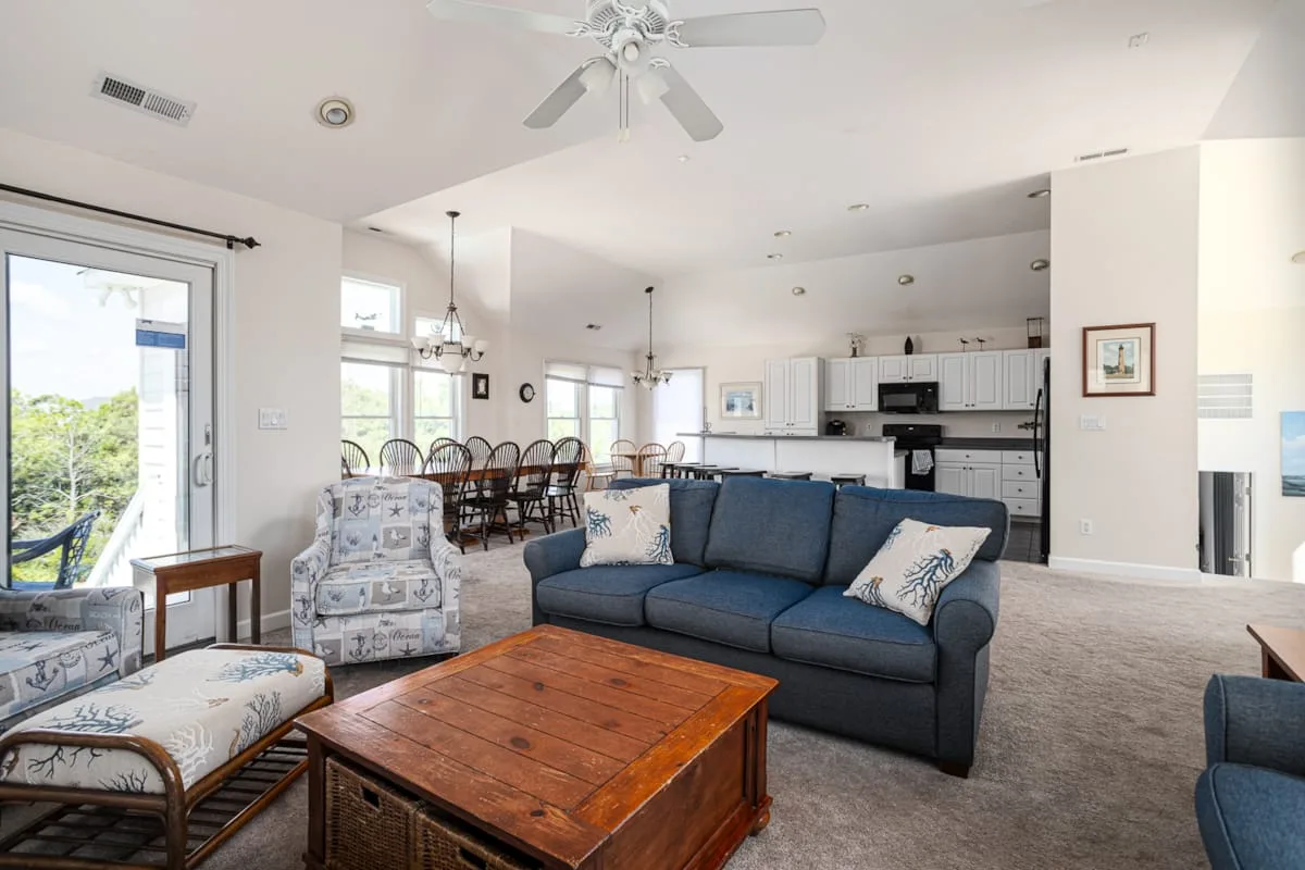 A bright living room with blue seating, a wooden coffee table, and an open kitchen.