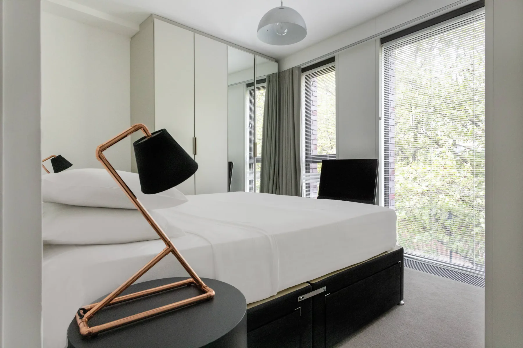 A bedroom with a neatly made bed beside large windows.