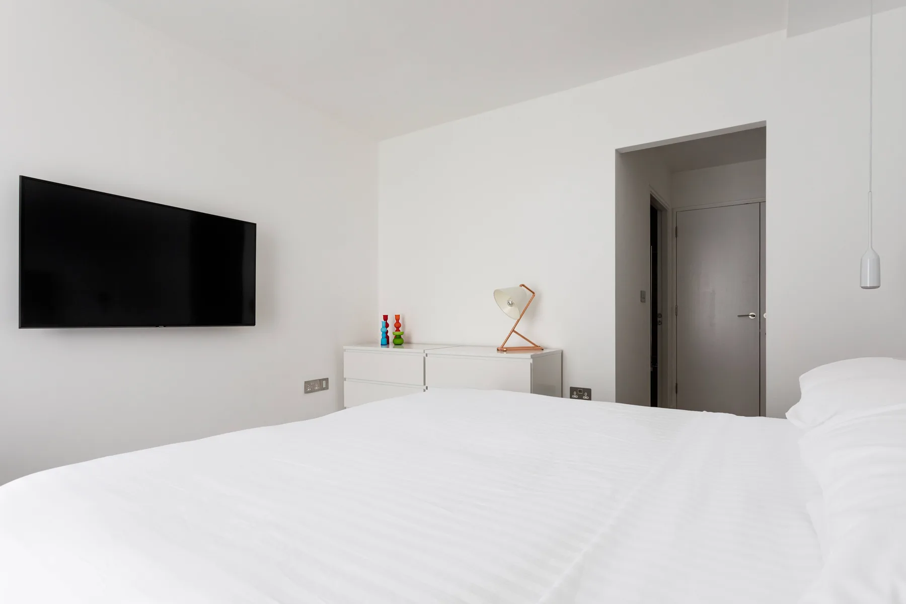 A bright bedroom with a white bed and a wall-mounted television.