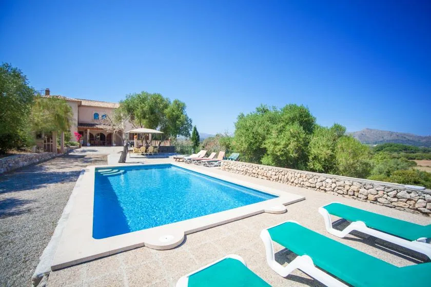 A swimming pool sits beside a stone wall, with lounge chairs along the edge.