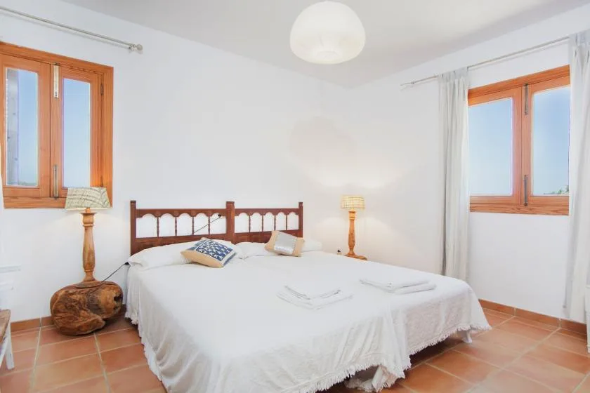 A bedroom with a double bed, wooden headboard, and two windows.