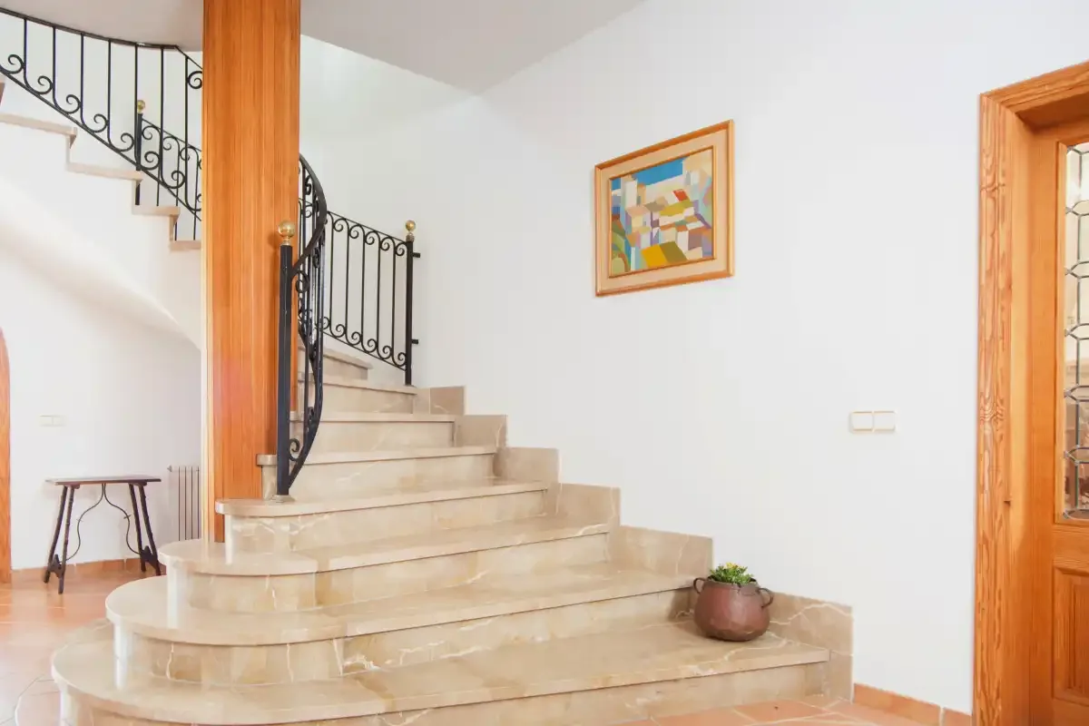A tiled staircase with a black metal railing rises beside a white wall.