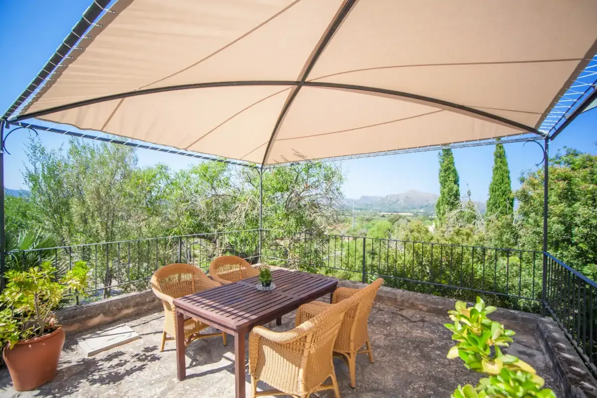 An outdoor dining area sits beneath a canopy, overlooking a garden and distant hills.