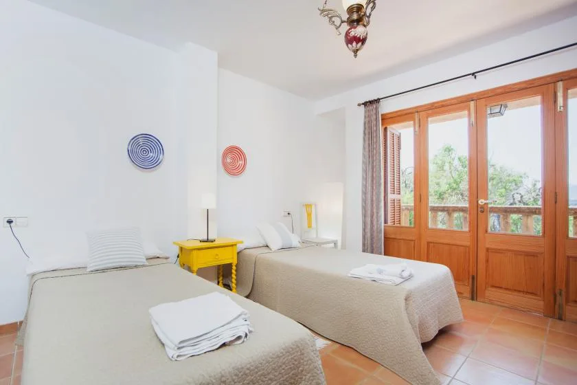 A bright bedroom with two beds and wooden doors opening onto a balcony.