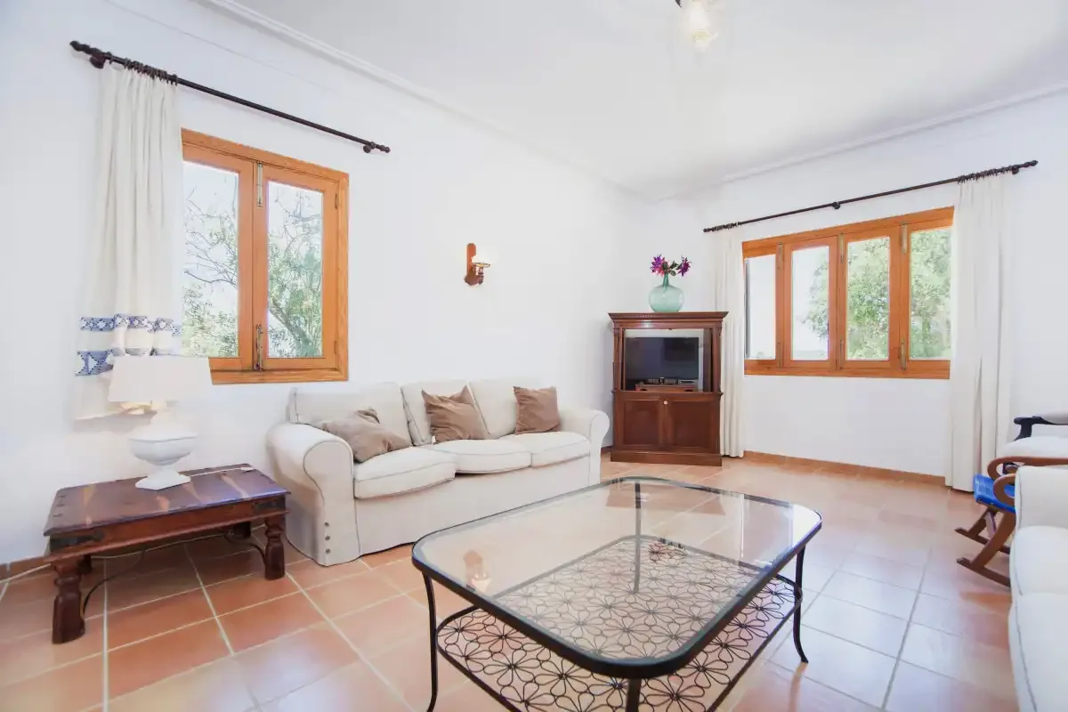 A bright living room with seating, a glass coffee table, and large windows.