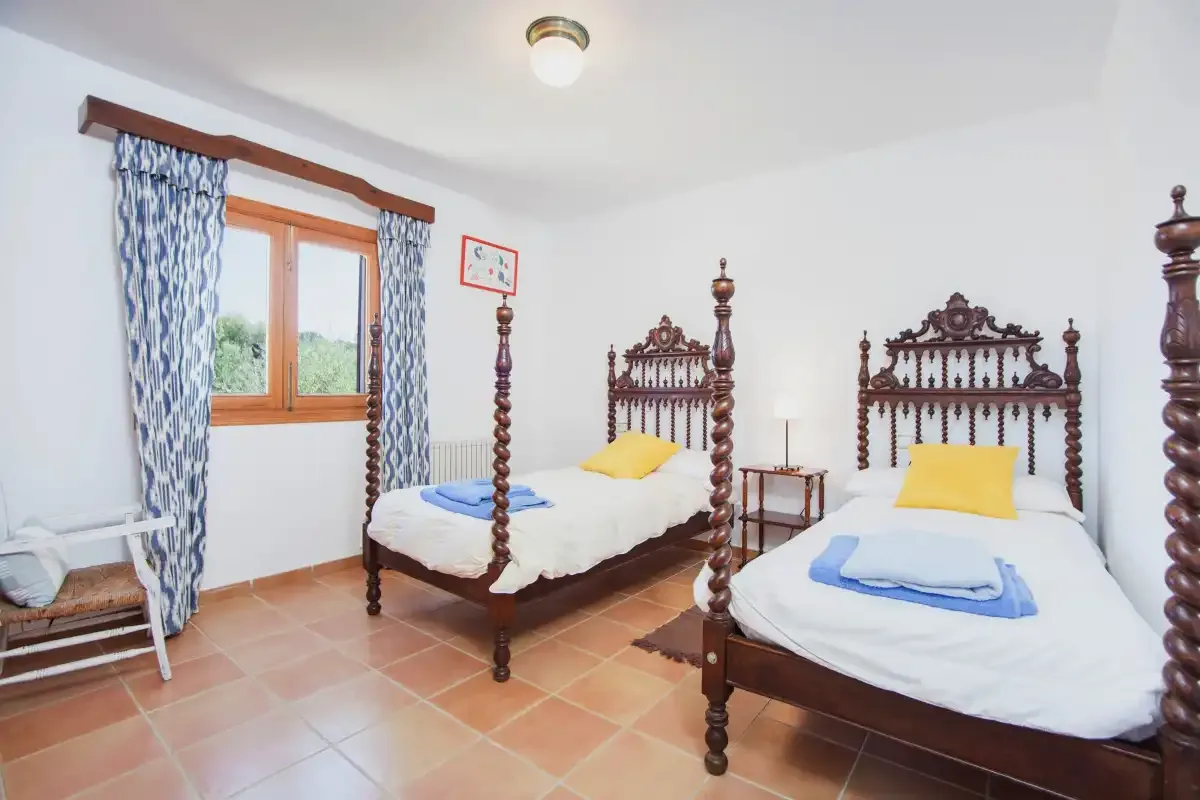 A bright bedroom with two beds, a window, and patterned curtains.
