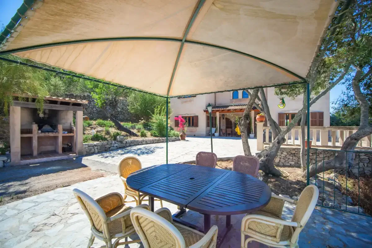 A shaded outdoor dining area has a table and seating beside a stone-paved courtyard.