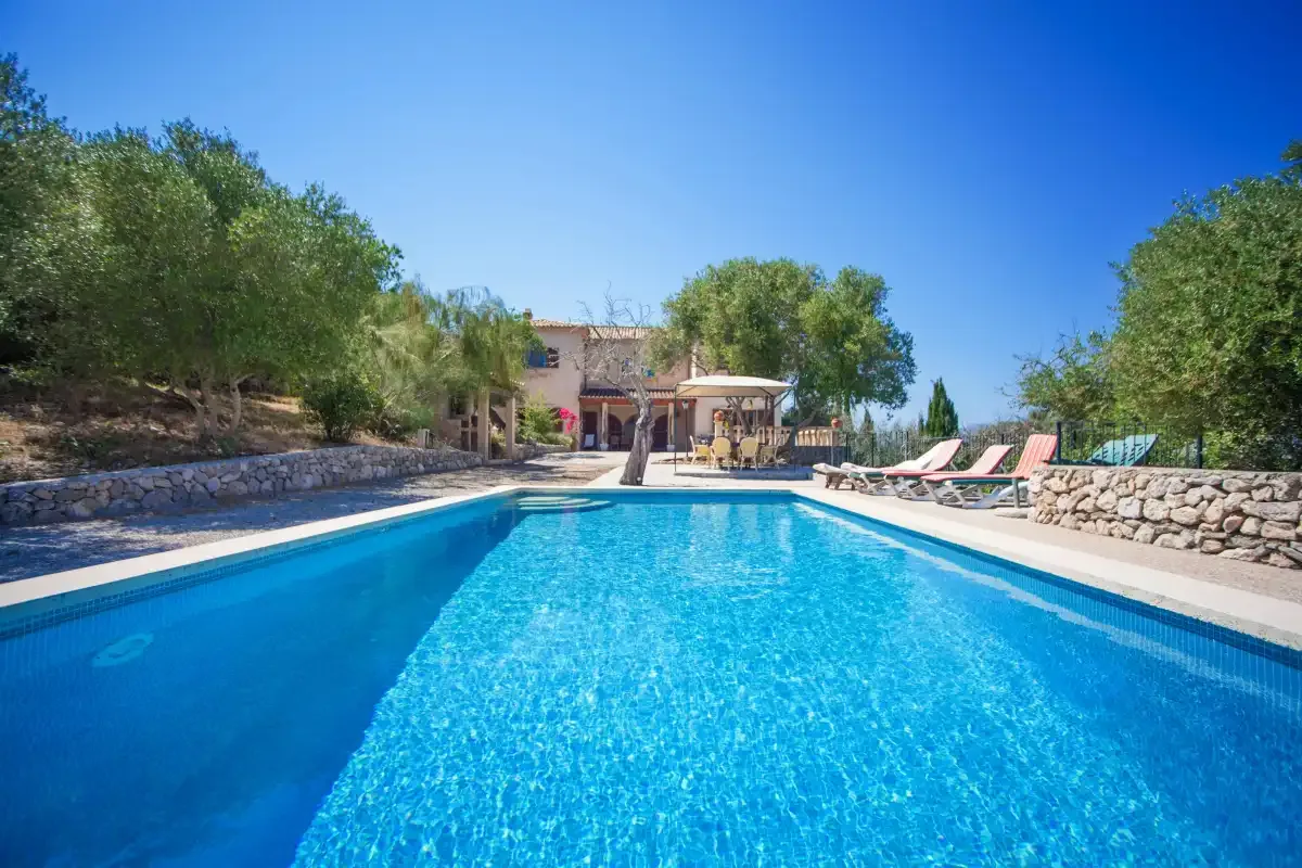 A swimming pool stretches toward a shaded seating area, with loungers along the side.