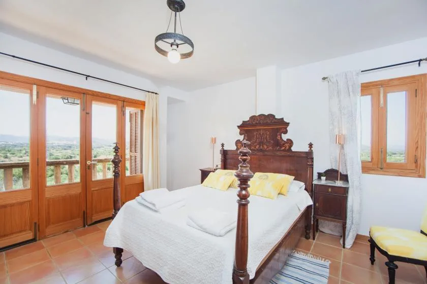 A bright bedroom with a wooden bed and large windows overlooking a green landscape.