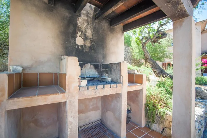 A covered outdoor cooking area with a built-in grill and tiled counters.