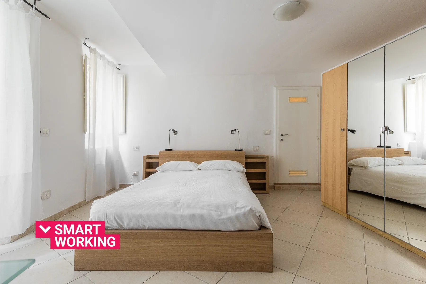 Un dormitorio luminoso con una cama, estantes laterales y puertas de armario con espejo.