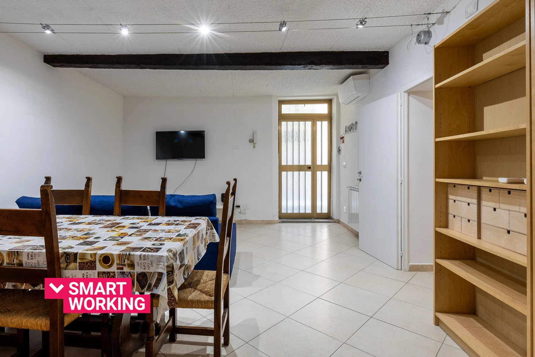 Un comedor y sala de estar con una mesa, asientos y un televisor en la pared.