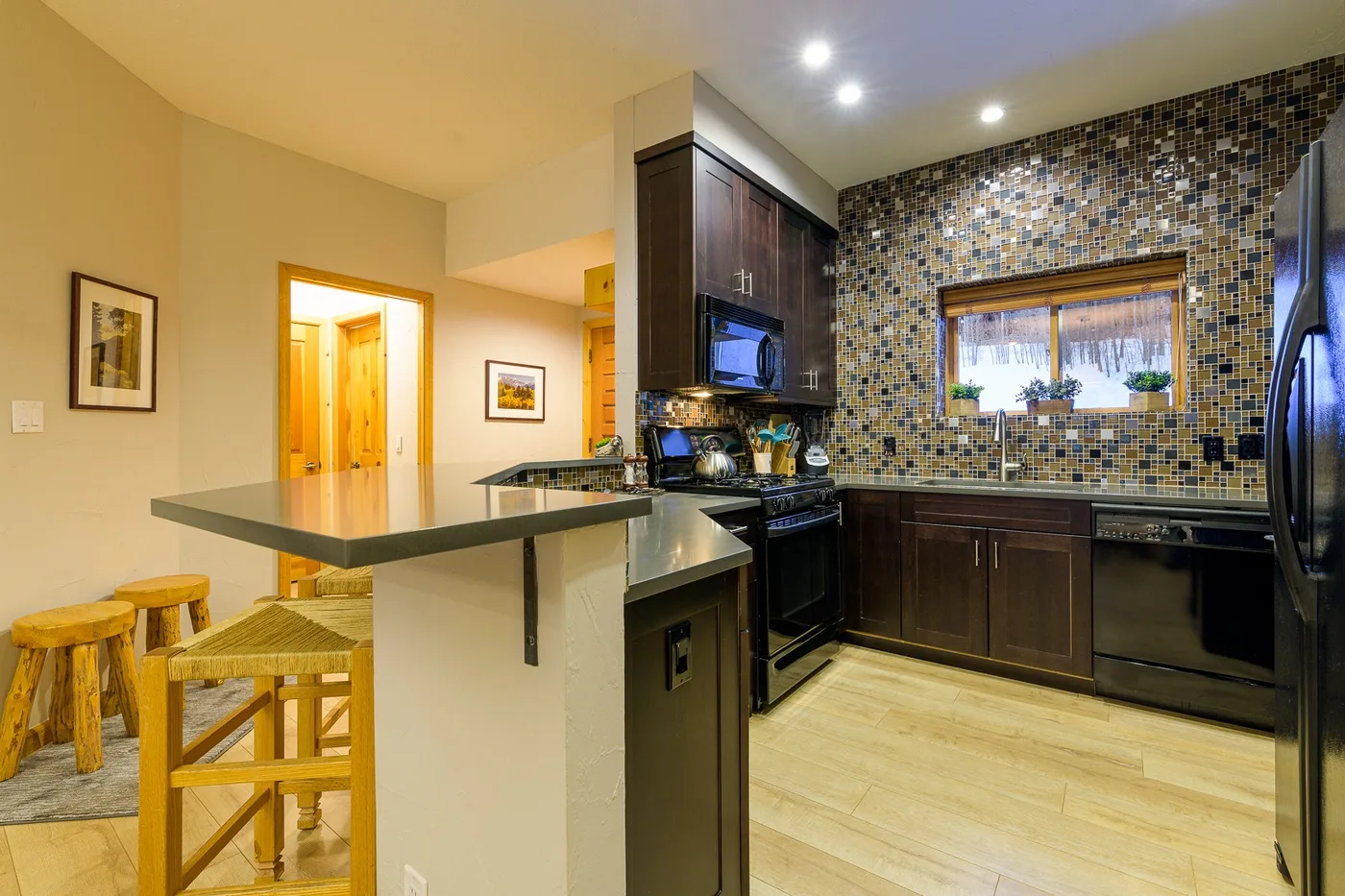 Una cocina con gabinetes oscuros, un salpicadero de azulejos y una barra con taburetes.