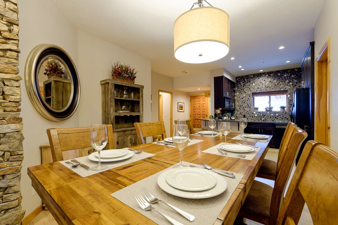Comedor con una larga mesa de madera puesta con platos junto a la cocina.