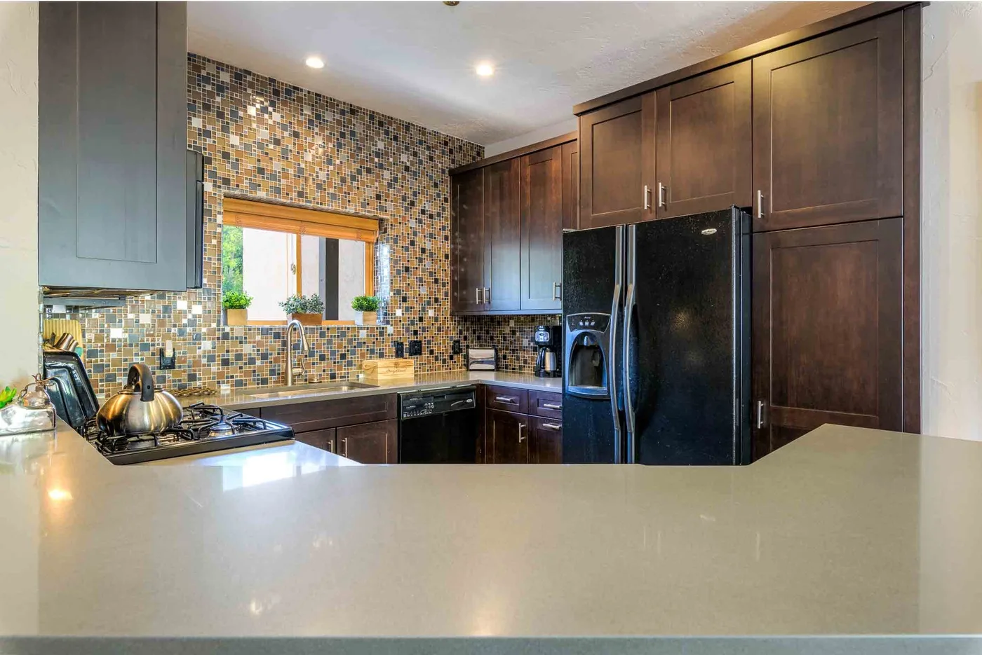 Una cocina con gabinetes oscuros, un salpicadero de azulejos y una amplia encimera clara.