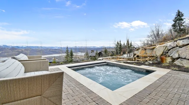 An outdoor hot tub sits on a paved patio overlooking a mountain landscape.