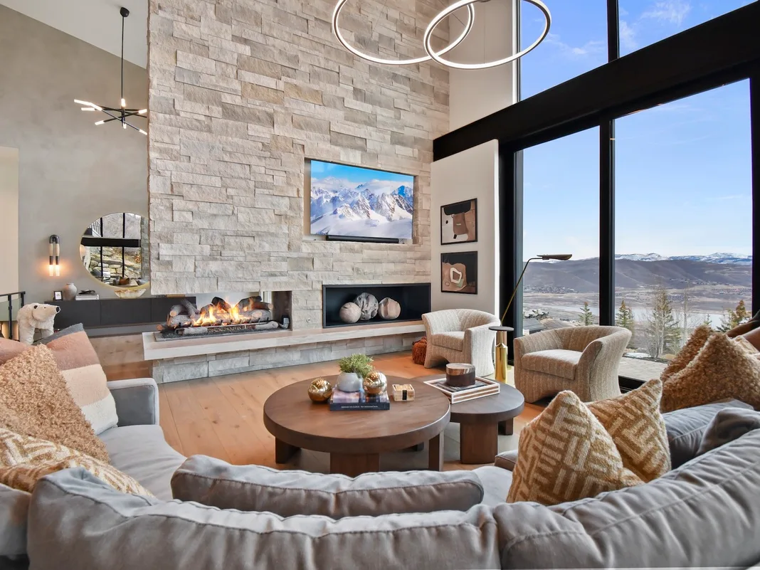 A bright living room with seating arranged around a fireplace and large windows.
