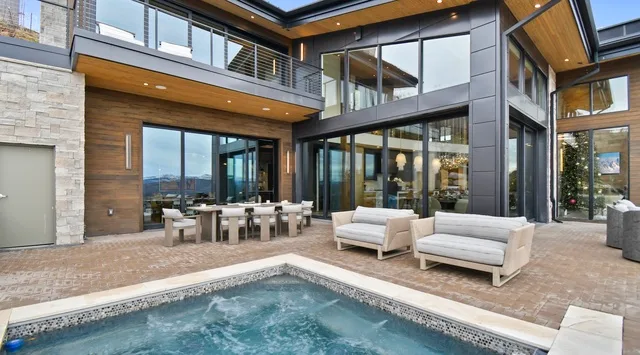 A modern house opens onto a stone patio with a swimming pool and outdoor seating.
