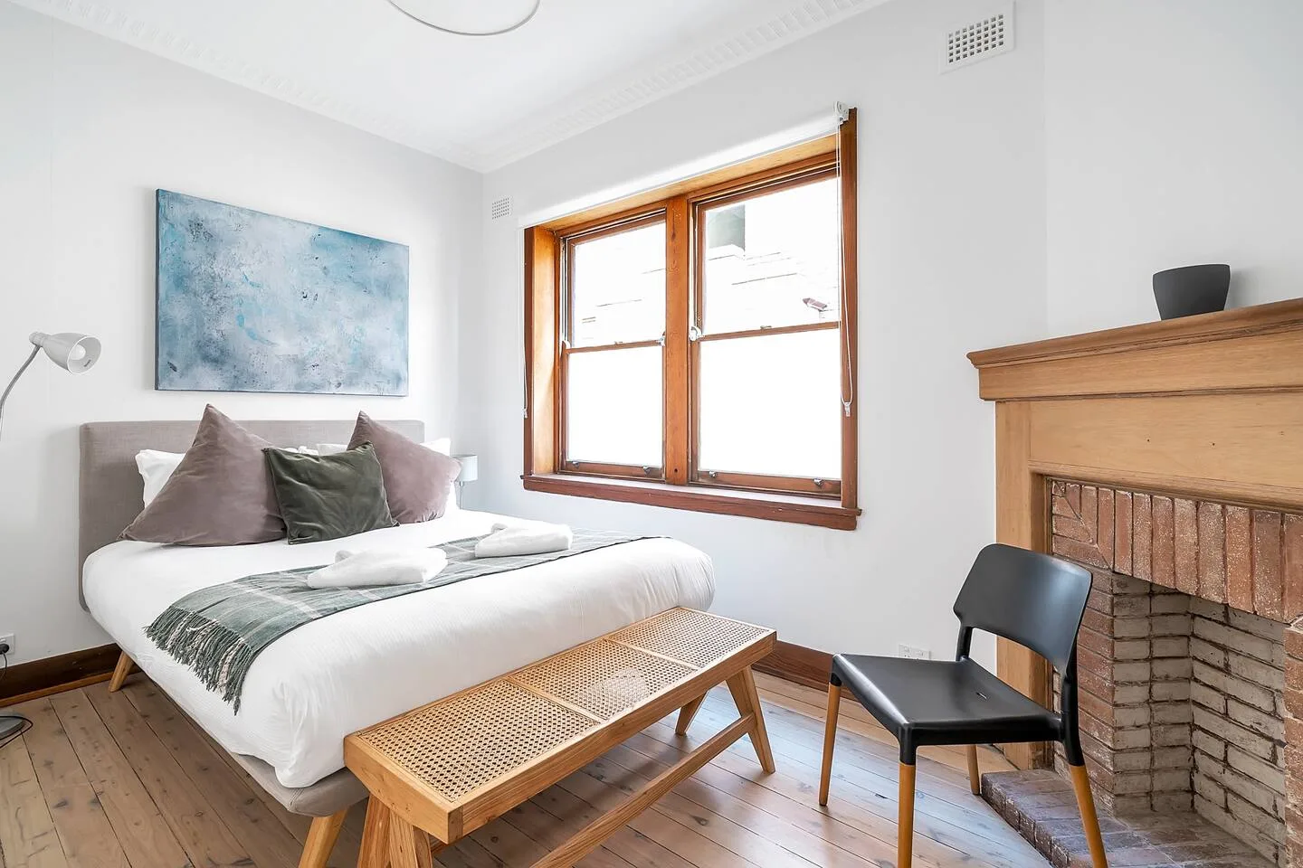 Un dormitorio con una cama, una obra de arte y un banco de madera junto a la ventana.