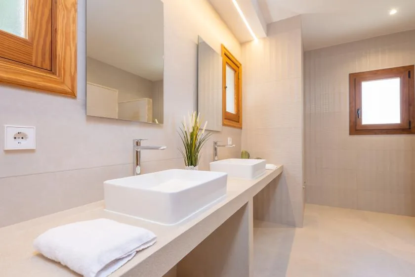 A bright bathroom with a long counter, two sinks, and wall mirrors.