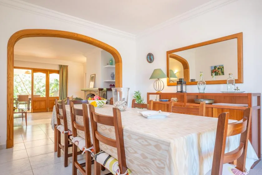 A dining room with a long table and wooden seating beside an arched doorway.
