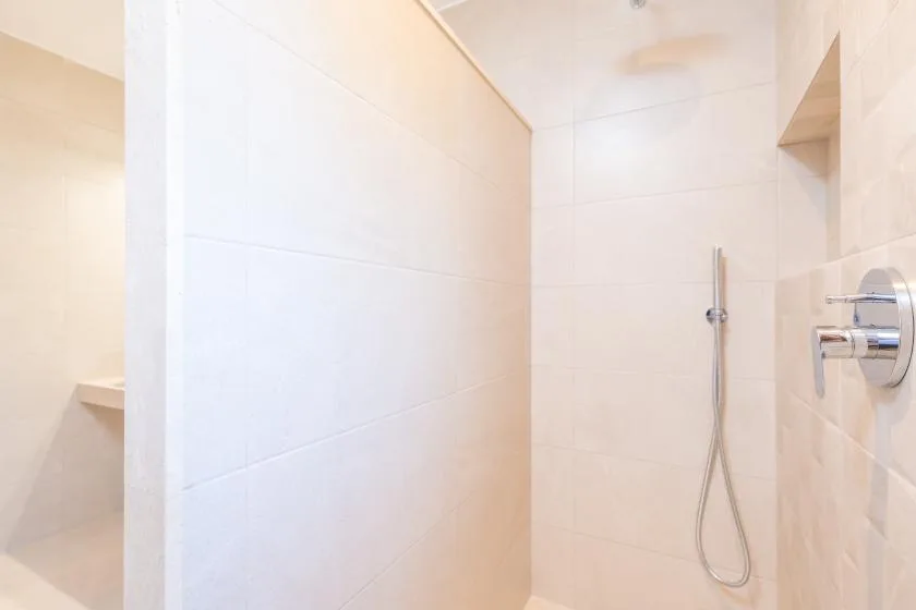 A tiled shower area with a wall-mounted showerhead and controls.
