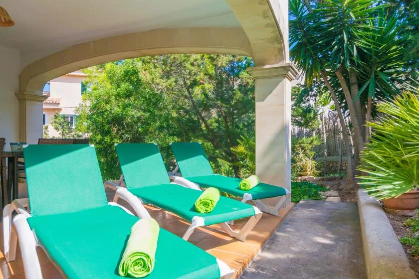 Un patio exterior sombreado con tumbonas turquesas y vistas a un jardín frondoso.