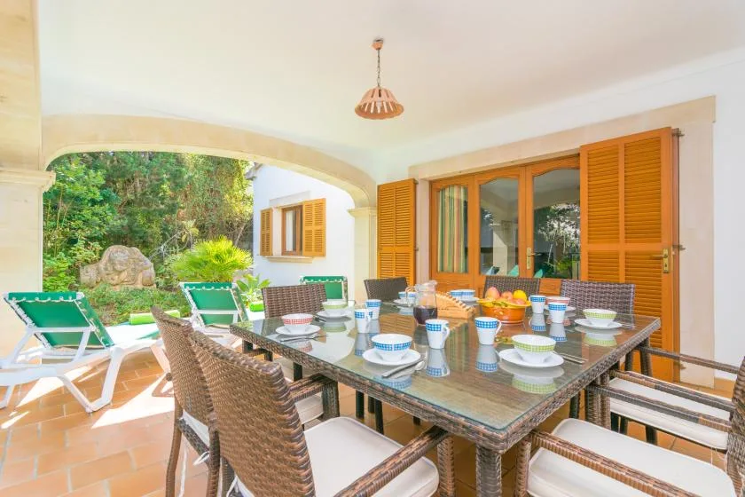 Comedor exterior cubierto con la mesa puesta y vistas al jardín.