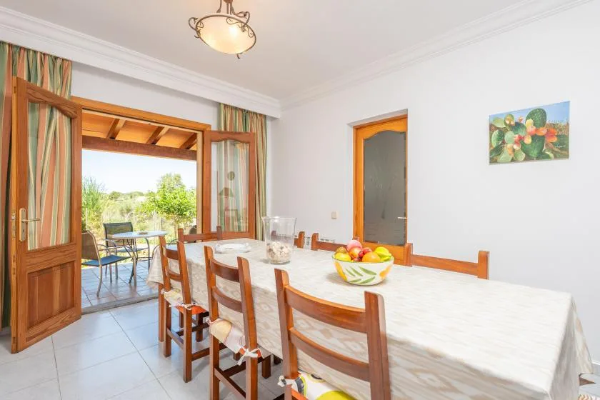 A dining room with a long table and open doors leading to a patio.