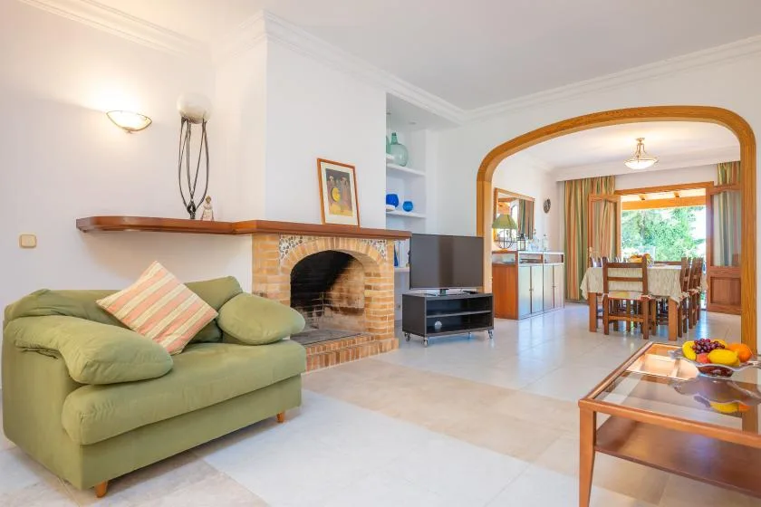 A living room opens into a dining area, with green seating beside a brick fireplace.