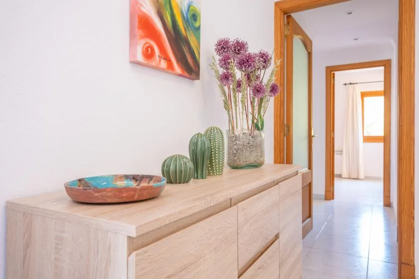 A hallway with a light wood console, decorative objects, and an open doorway.
