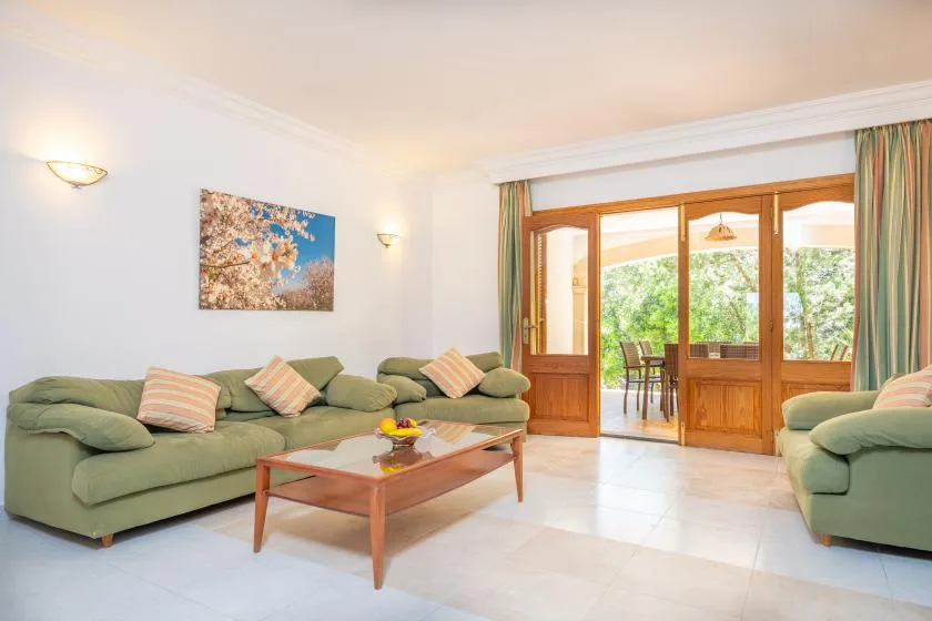 A living room with green seating and wooden doors opening onto a bright outdoor area.