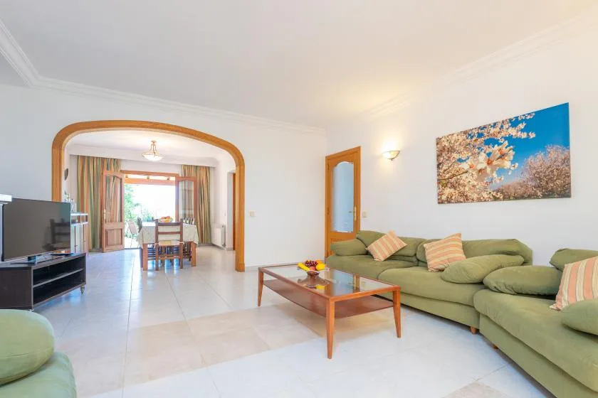 A living room with green seating, a coffee table, and a dining area beyond the archway.