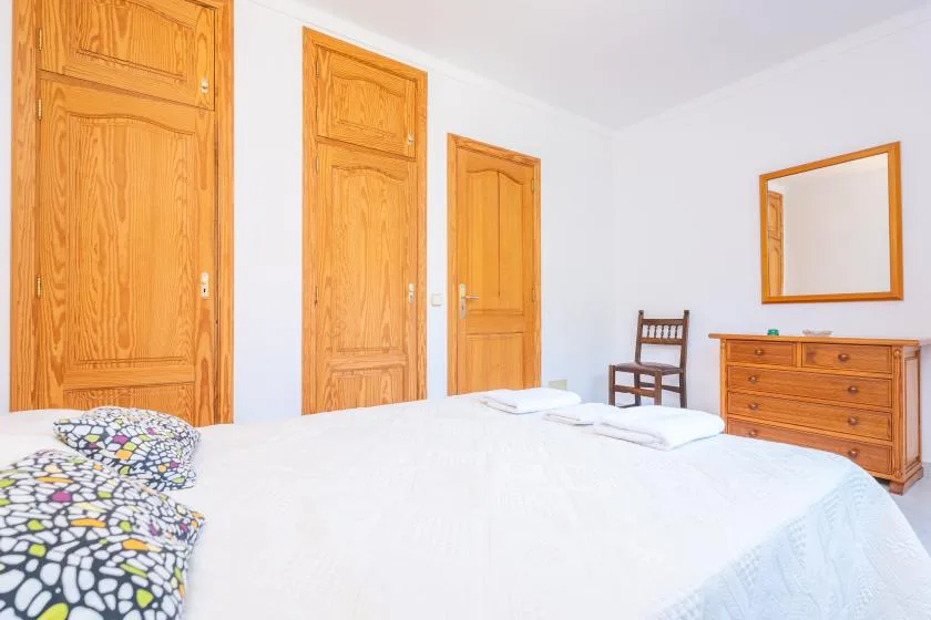 A bright bedroom with a neatly made bed and wooden furniture.