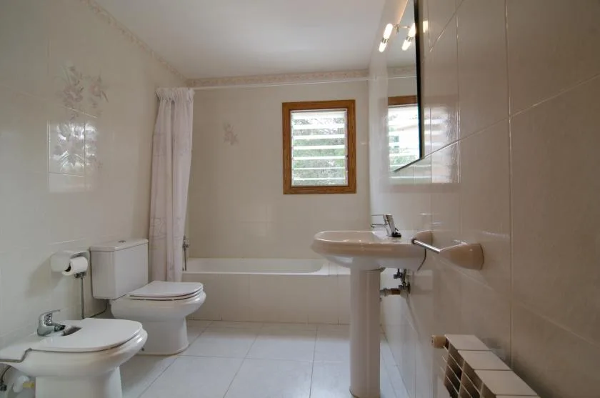A tiled bathroom with a bathtub, toilet, and pedestal sink.