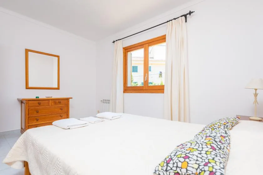 A bright bedroom with a large bed, wooden dresser, and curtained window.