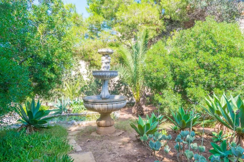 A stone fountain stands among leafy plants in a garden.